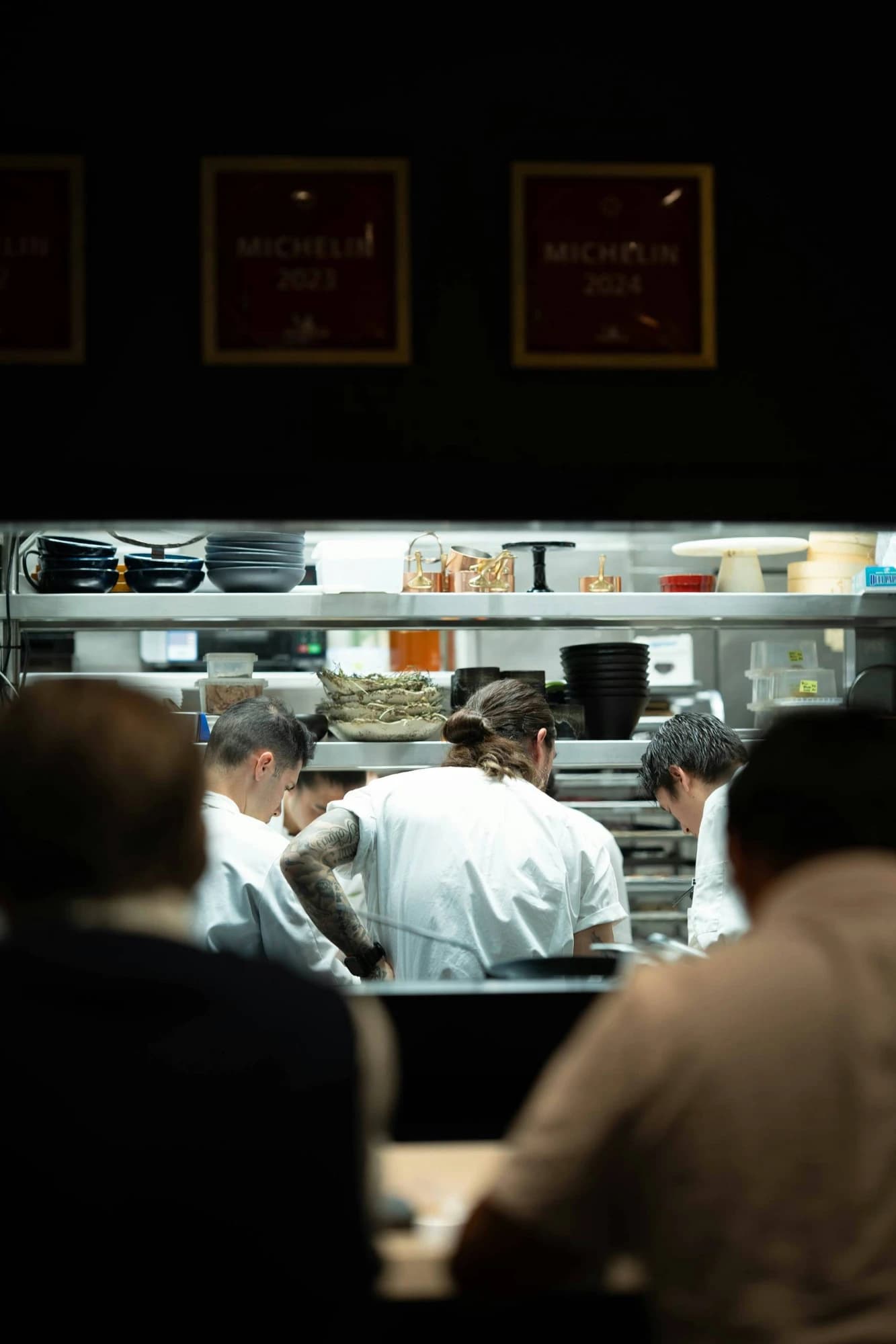 Chefs working the pass in an open kitchen, seen from the dining counter